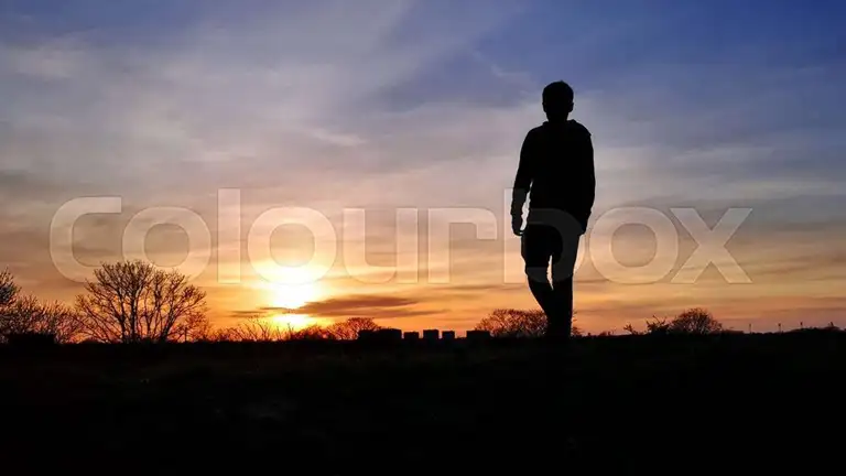 Mand som går mod solnedgang i horisont